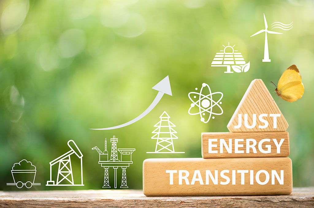© Adobe Stock | wasanajai Drei gestlapelte Holzklötze mit der Aufschrift "Just Energy Transition" vor grünem Hintergrund. Links daneben der Verlauf der Energiewende dargstellt durch Grafikelemente der Energiegewinnungsarten im Verlauf der Zeit.