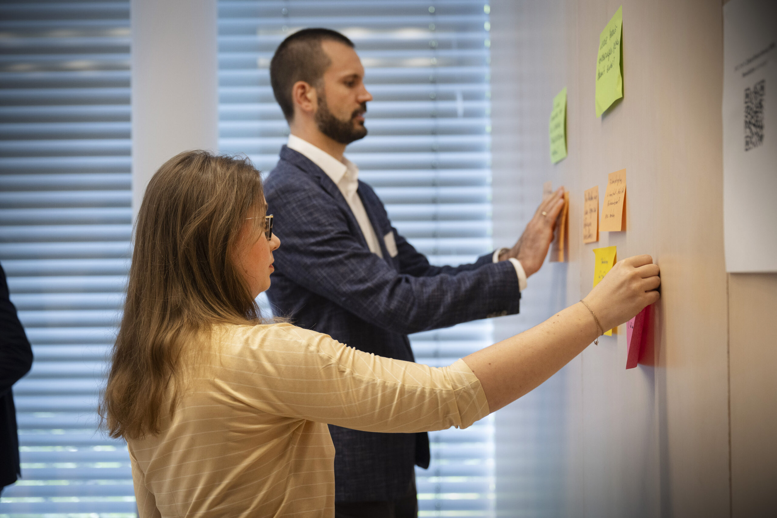 Eine Frau und ein Mann befestigten bunte, beschriftete Post-Its an einer Wand.