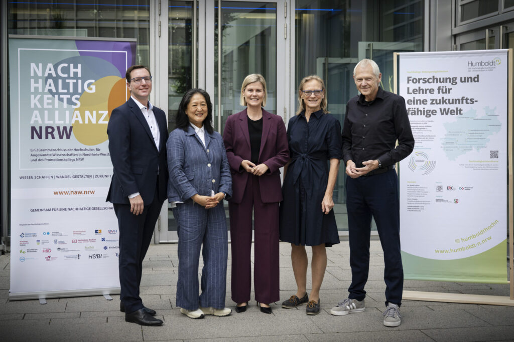 Drei Frauen und zwei Männer stehen vor einer Glasfront und lächeln in die Kamera, links und rechts von ihnen steht jeweils ein Roll-Up.