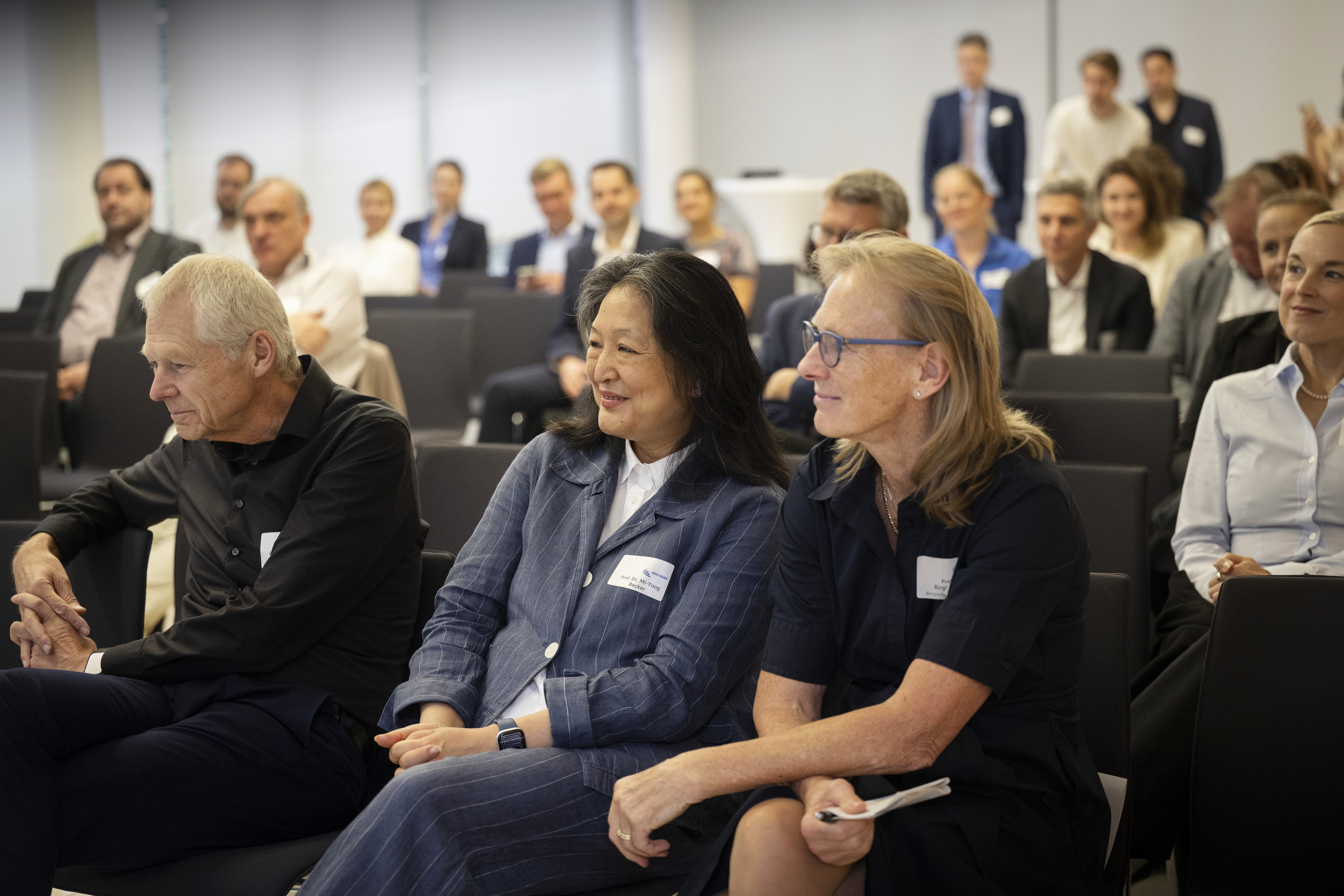 Foto von einem Publikum, das interessiert das Bühnenprogramm verfolgt. In der ersten Reihe sitzen zwei Frauen und ein Mann.